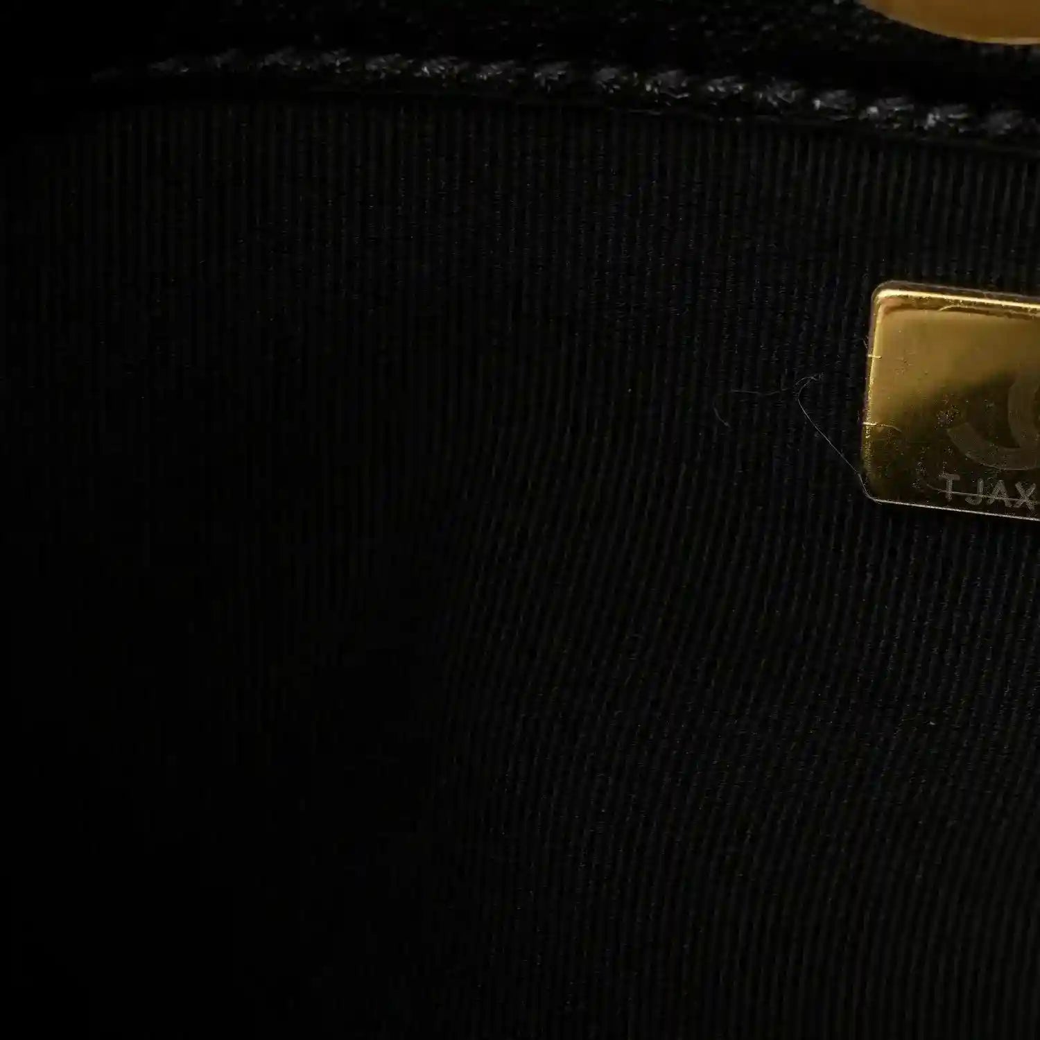 Chanel embossed hardware patch on black lining fabric near a gold edge
