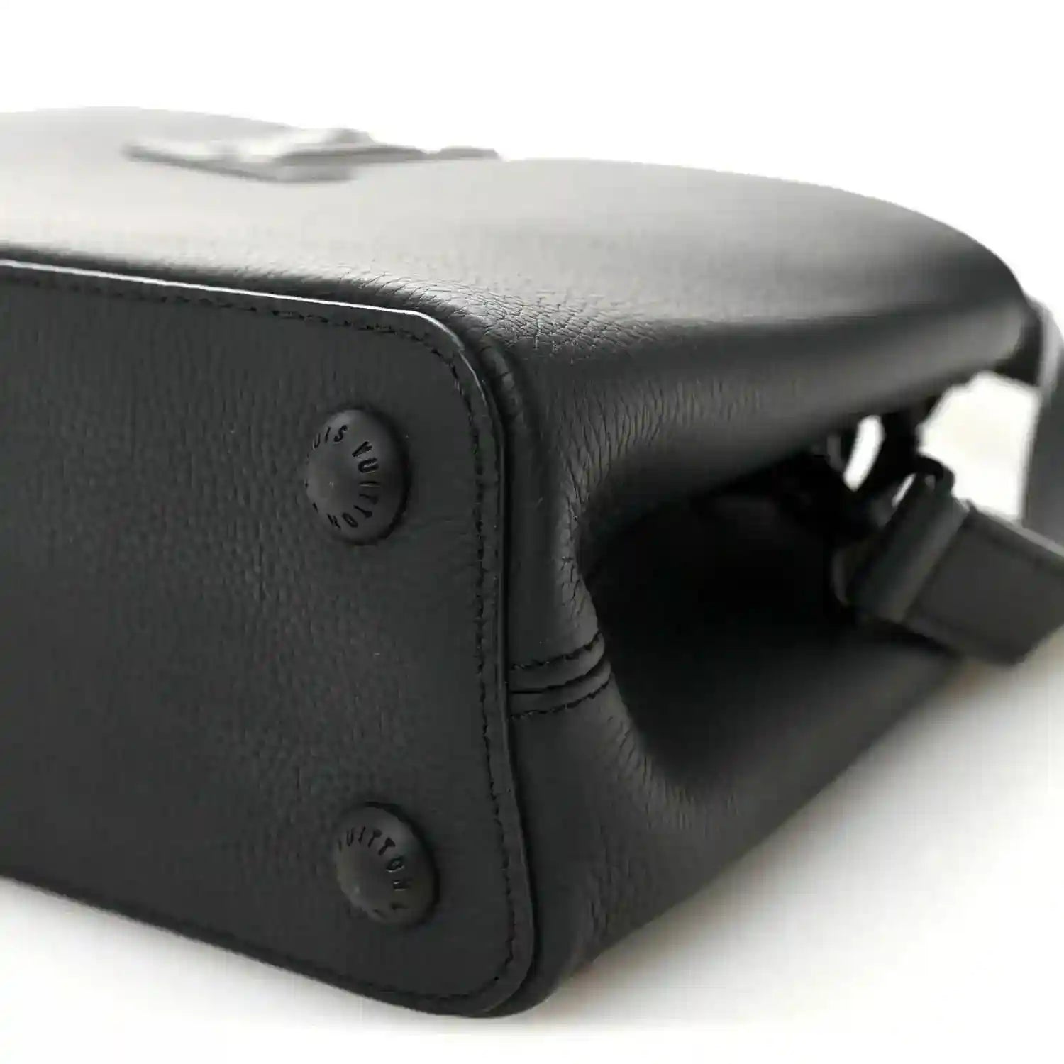 Matte black leather handbag corner with embossed button and strap hardware