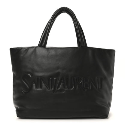 SAINT LAURENT lambskin wide puffer tote in black with embossed logo on front.