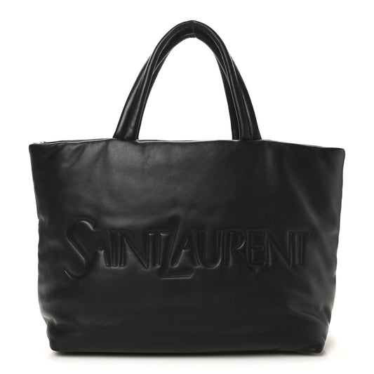 SAINT LAURENT lambskin wide puffer tote in black with embossed logo on front.