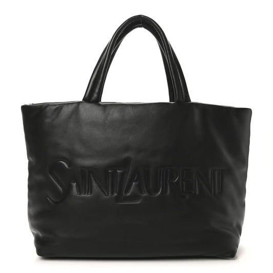 SAINT LAURENT lambskin wide puffer tote in black with embossed logo on front.