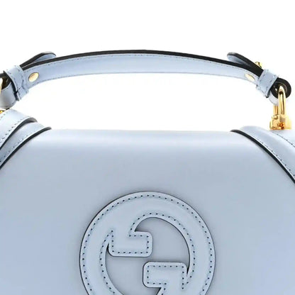 Light blue Gucci logo emblem on the front of a medium top-handle bag