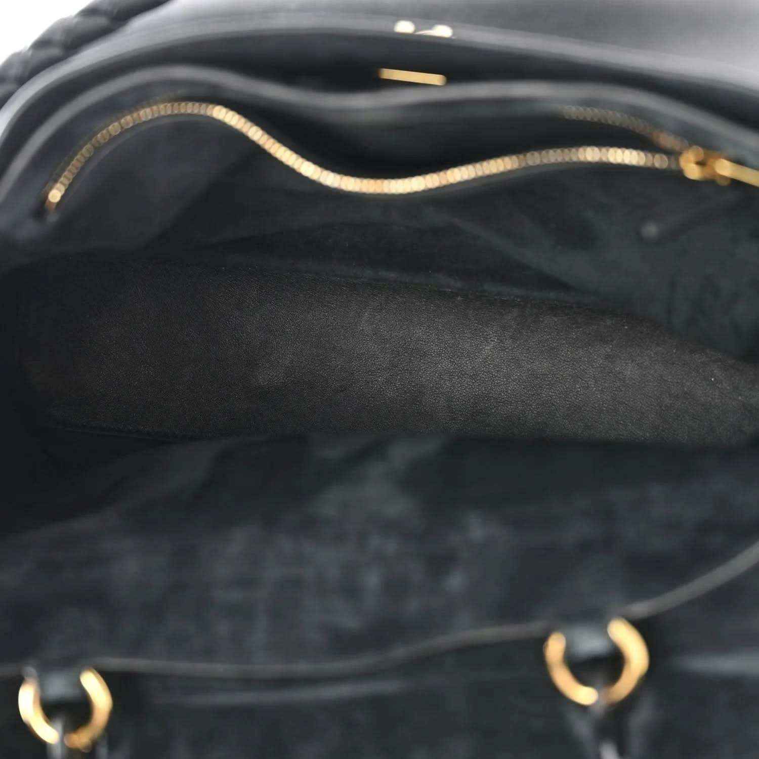 Close-up of black leather interior with gold-toned chain strap and stitched detail.