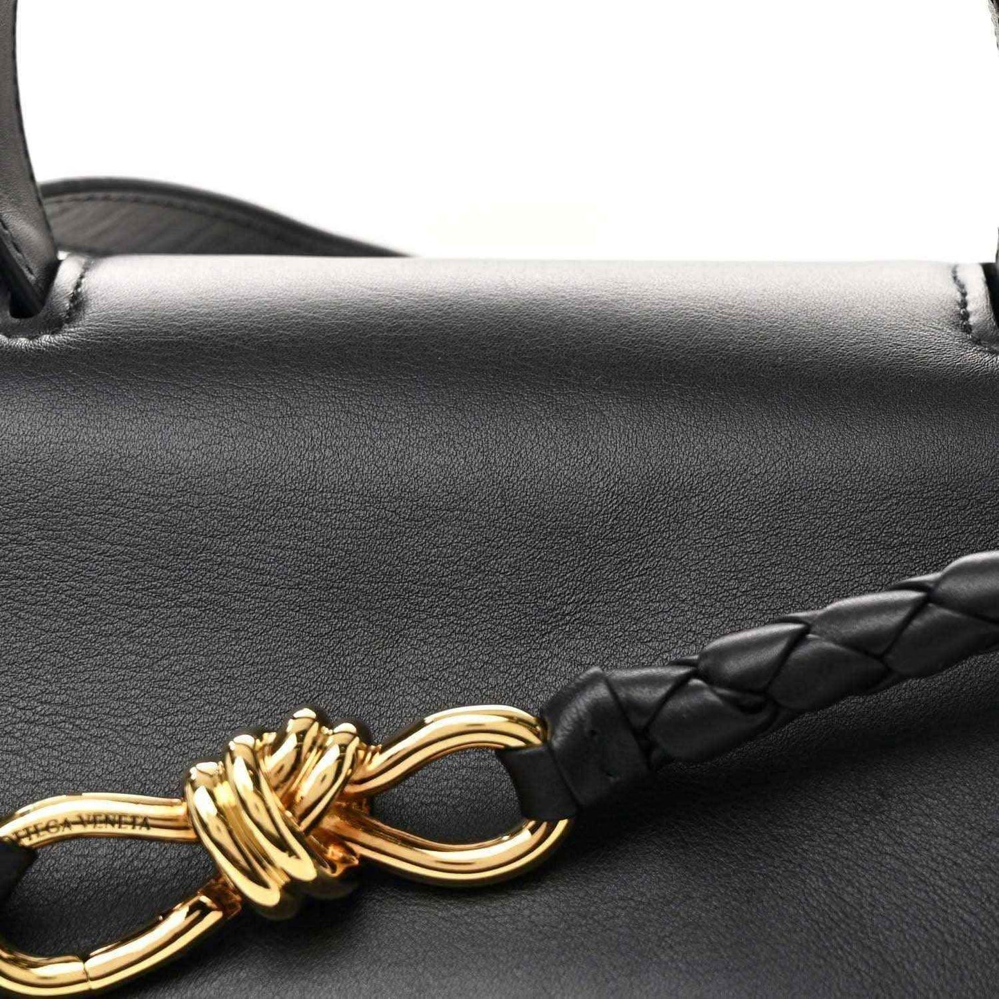 Gold knot clasp detail on black leather with braided strap section.