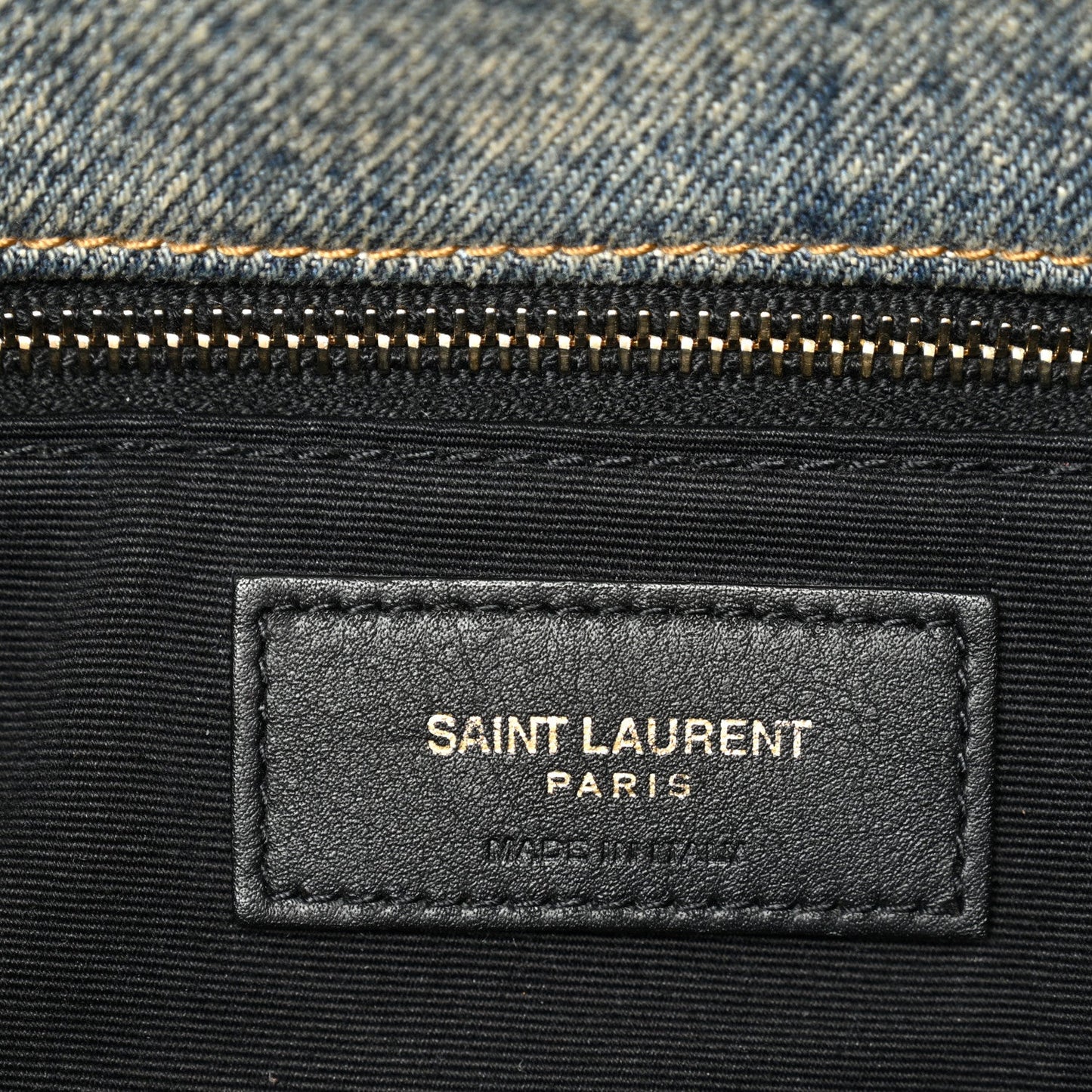 Black leather brand label reading SAINT LAURENT PARIS on denim satchel