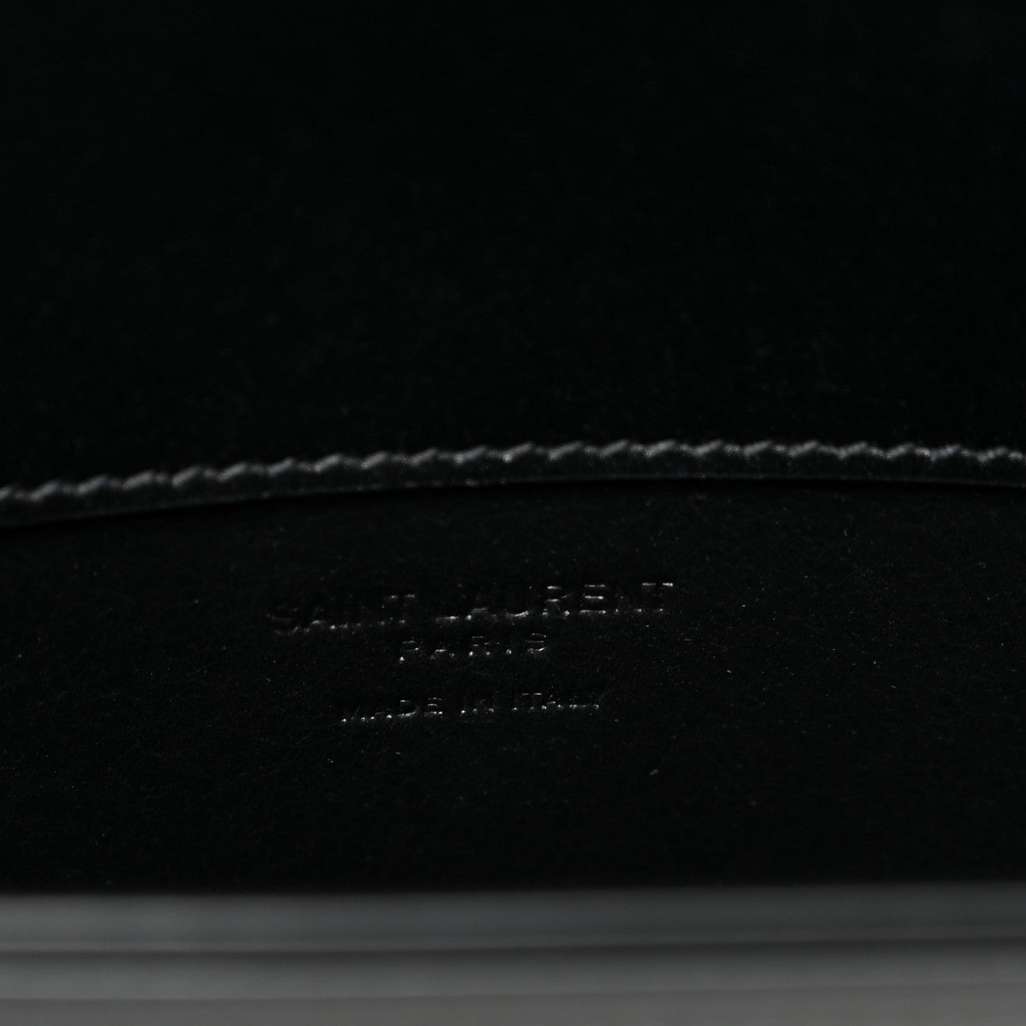 Black leather crossbody bag interior base with debossed brand text and stitching.