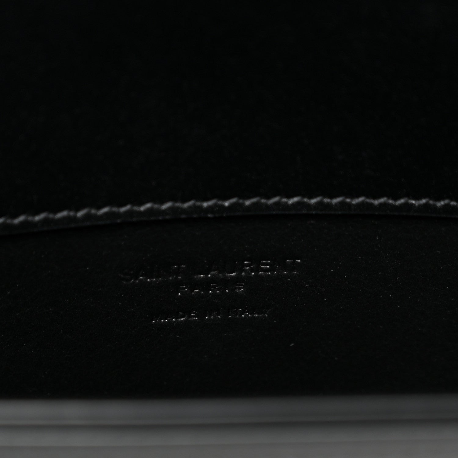 Black leather crossbody bag interior base with debossed brand text and stitching.
