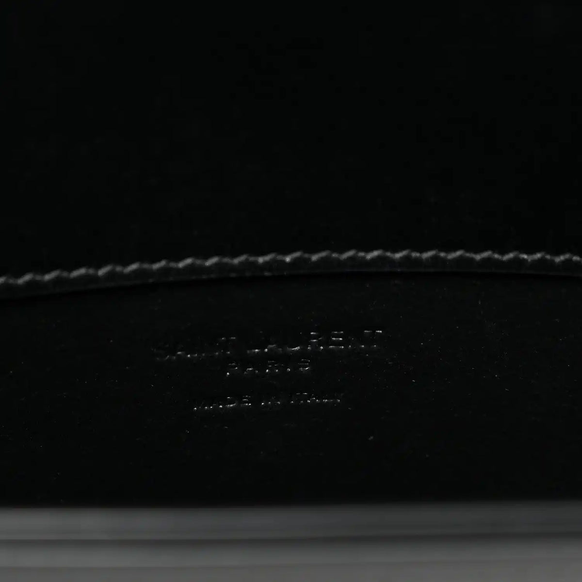 Black leather crossbody bag interior base with debossed brand text and stitching.