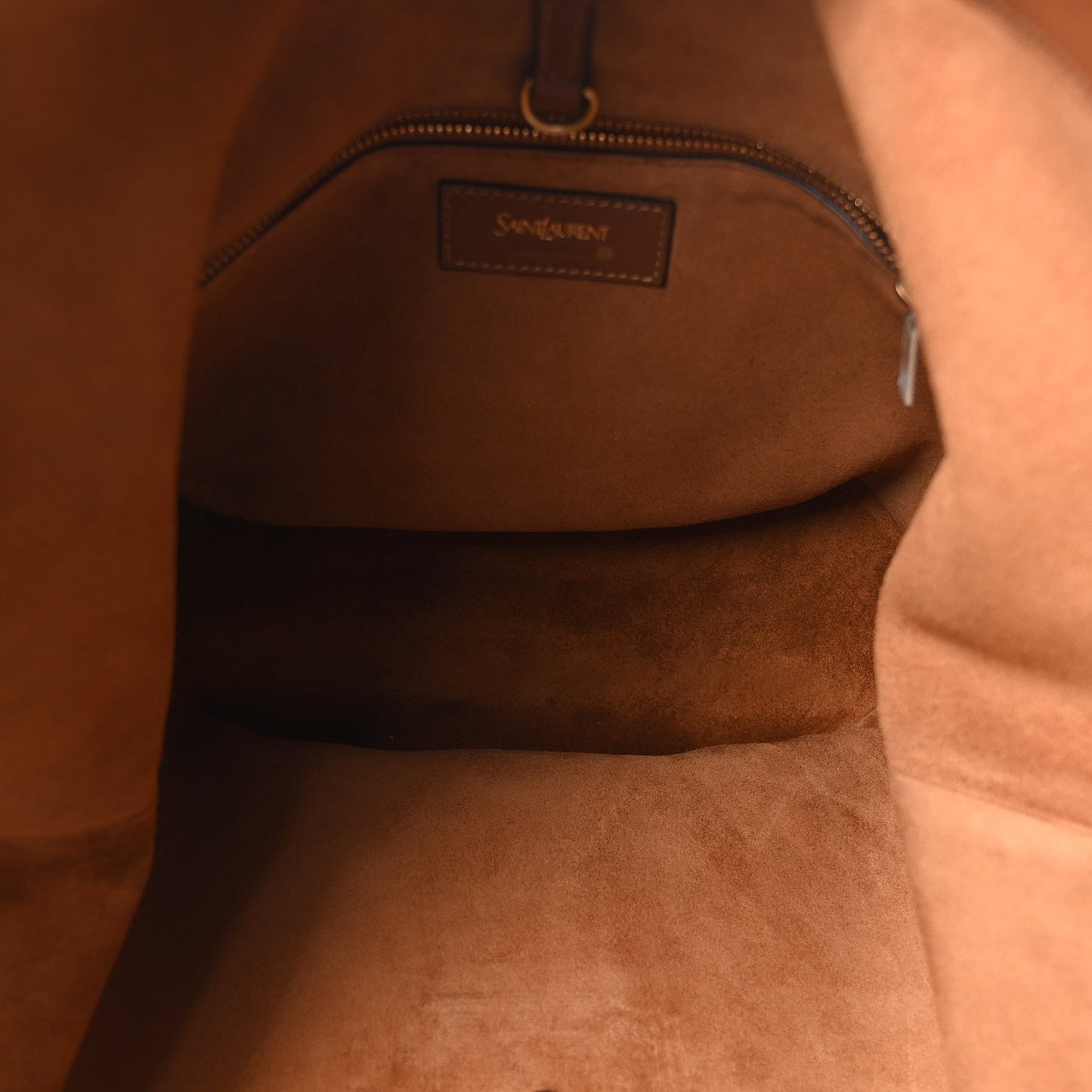 Inside view of a tan-brown leather tote with zip pocket and stitched logo label