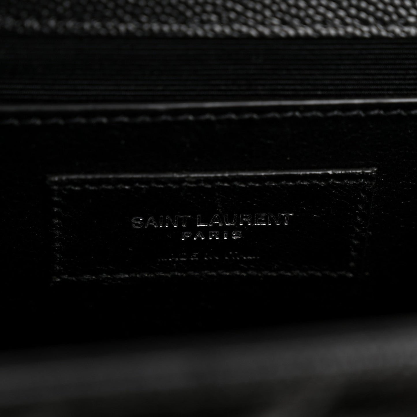 Black leather satchel label with embossed SAINT LAURENT text