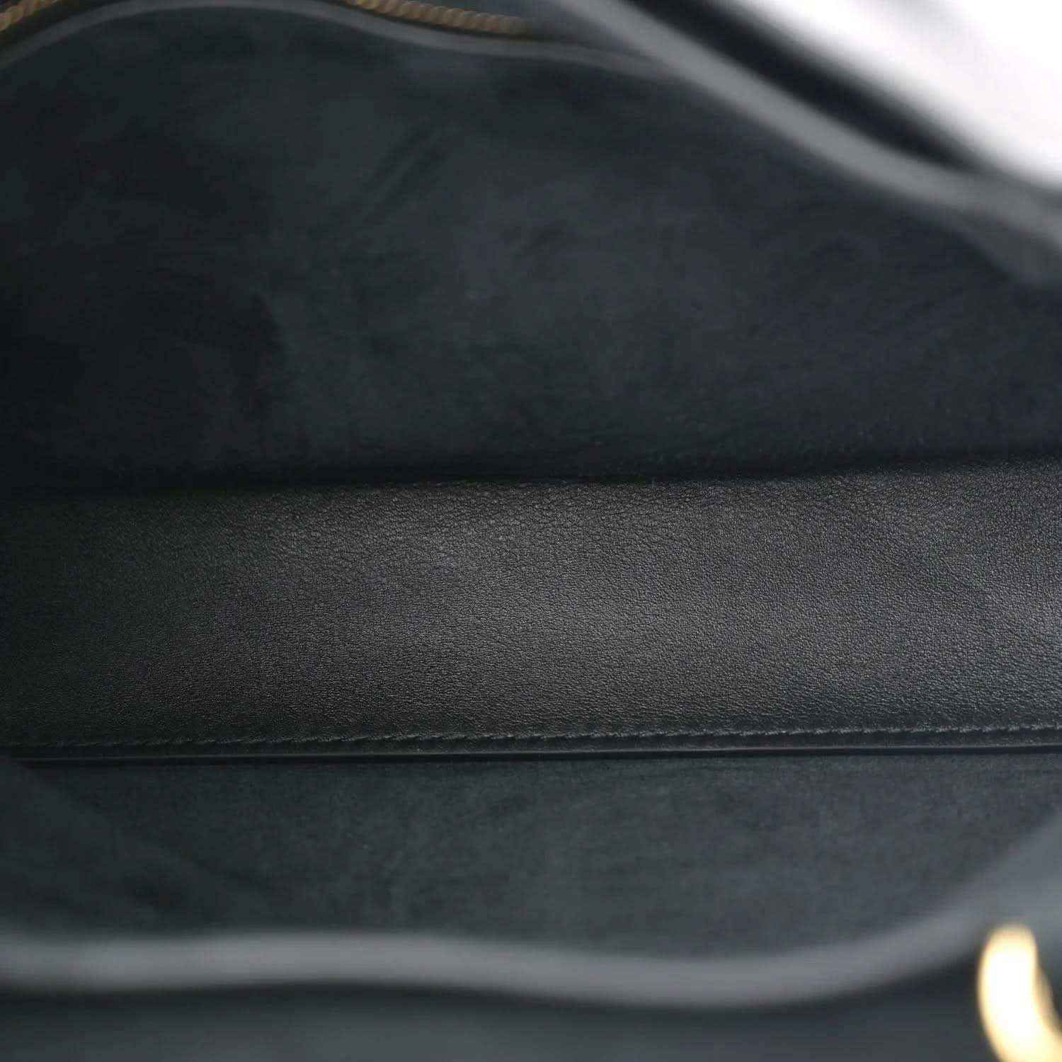 Black leather bag close-up showing smooth panel and subtle stitching seam.