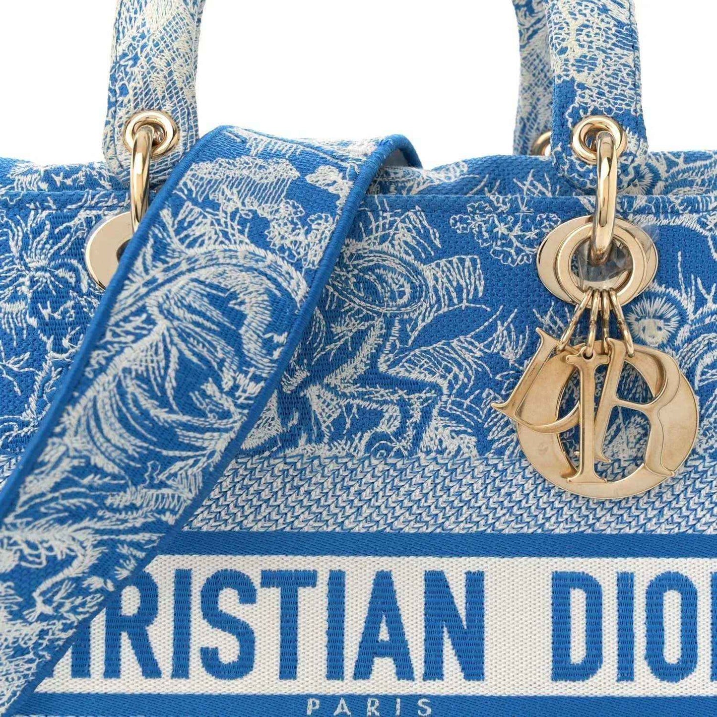 Blue embroidered tote bag close-up with Dior-Paris logo and gold charm hardware.