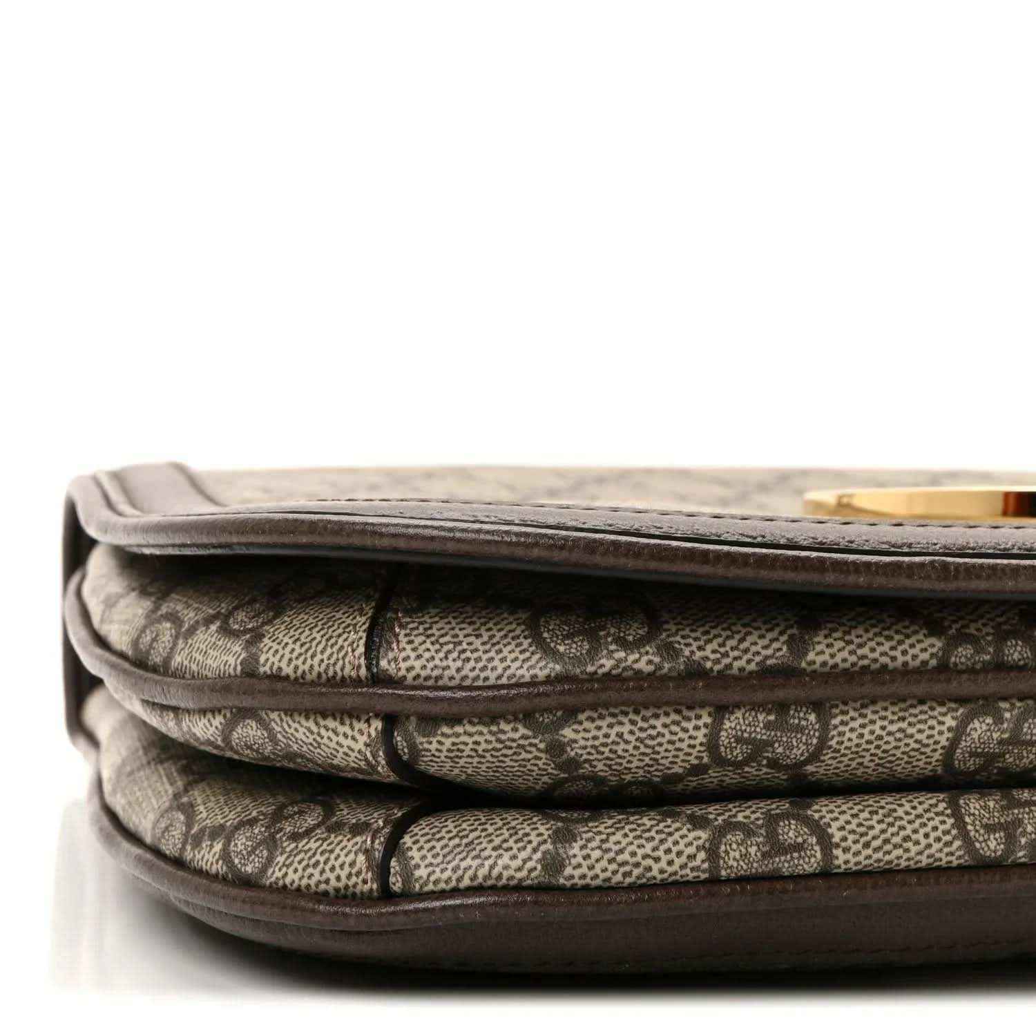 Folded view of beige GG monogram canvas with dark leather edging along the seam