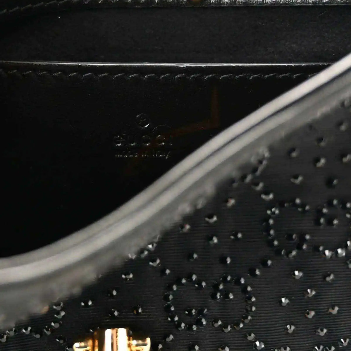 Close-up of black embossed monogram-style pattern on hobo bag with stitched trim.