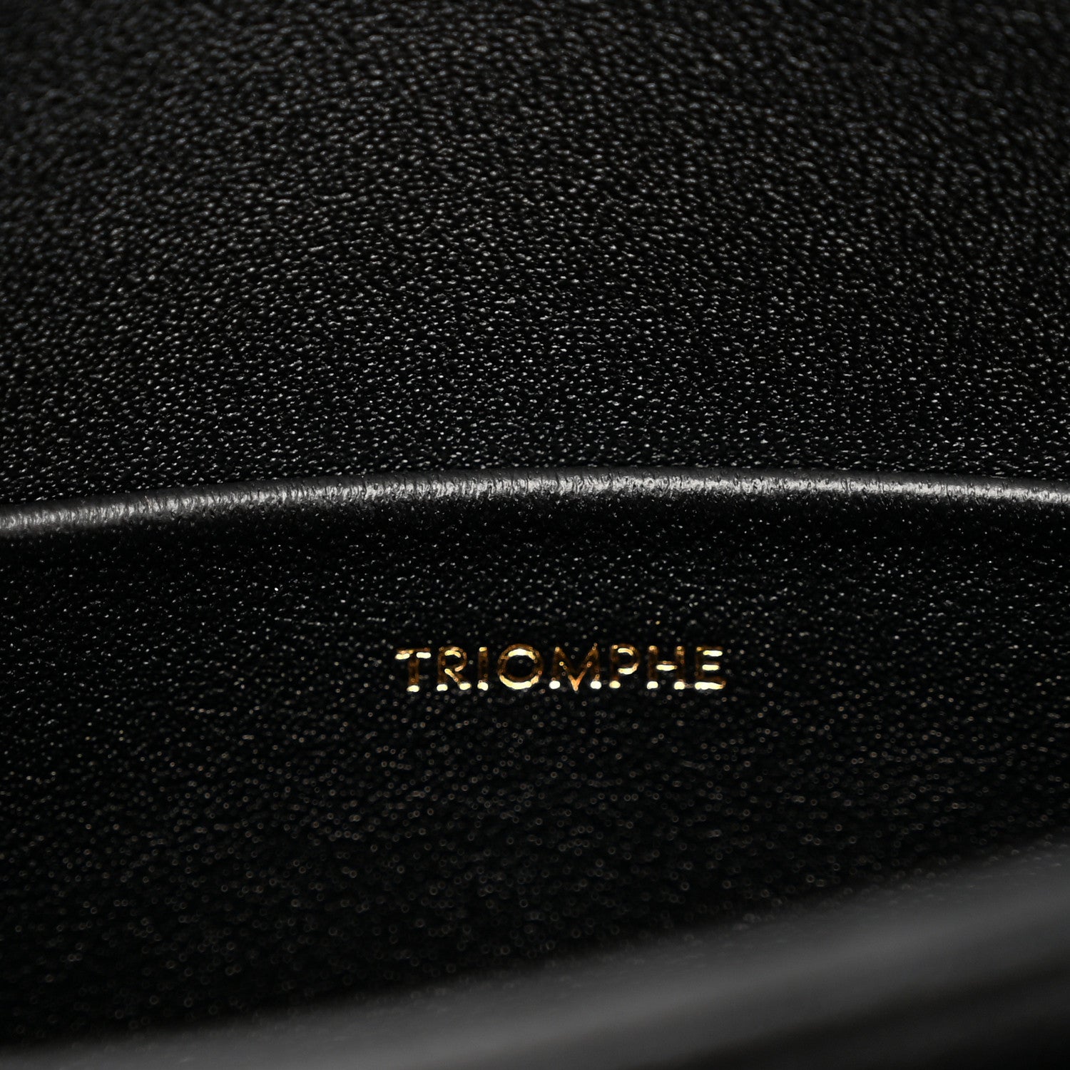 Black leather bag surface with 'TRIOMPHE' embossed lettering and fine grain texture.