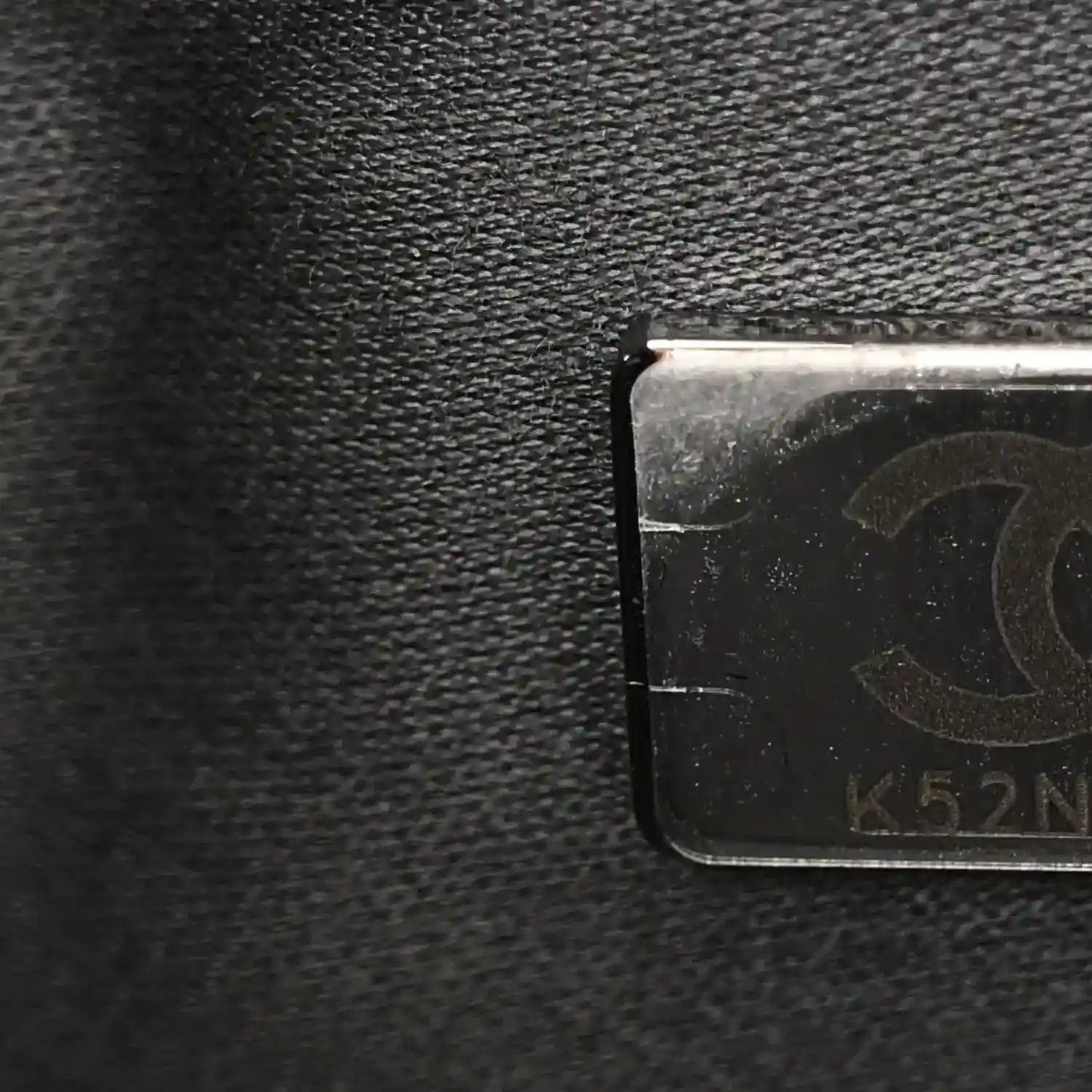 Chanel leather close-up with embossed stamp and metal tag on dark caviar surface