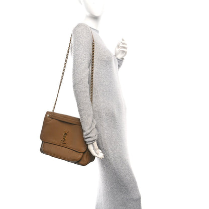 Small chain crossbody satchel held by model, grained dark cork leather.