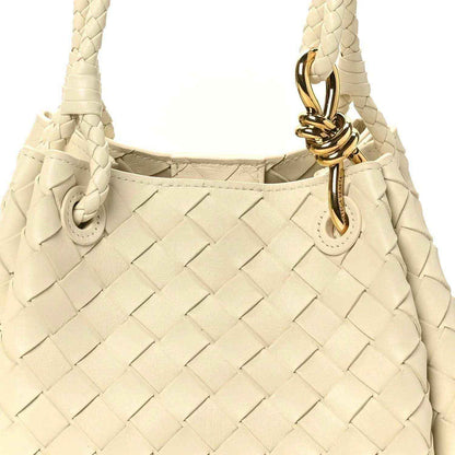 Light cream woven shoulder bag close-up with gold clasp and braided strap ends