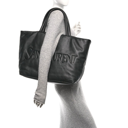 Black lambskin wide puffer tote with embossed logo, top handles, and side view.