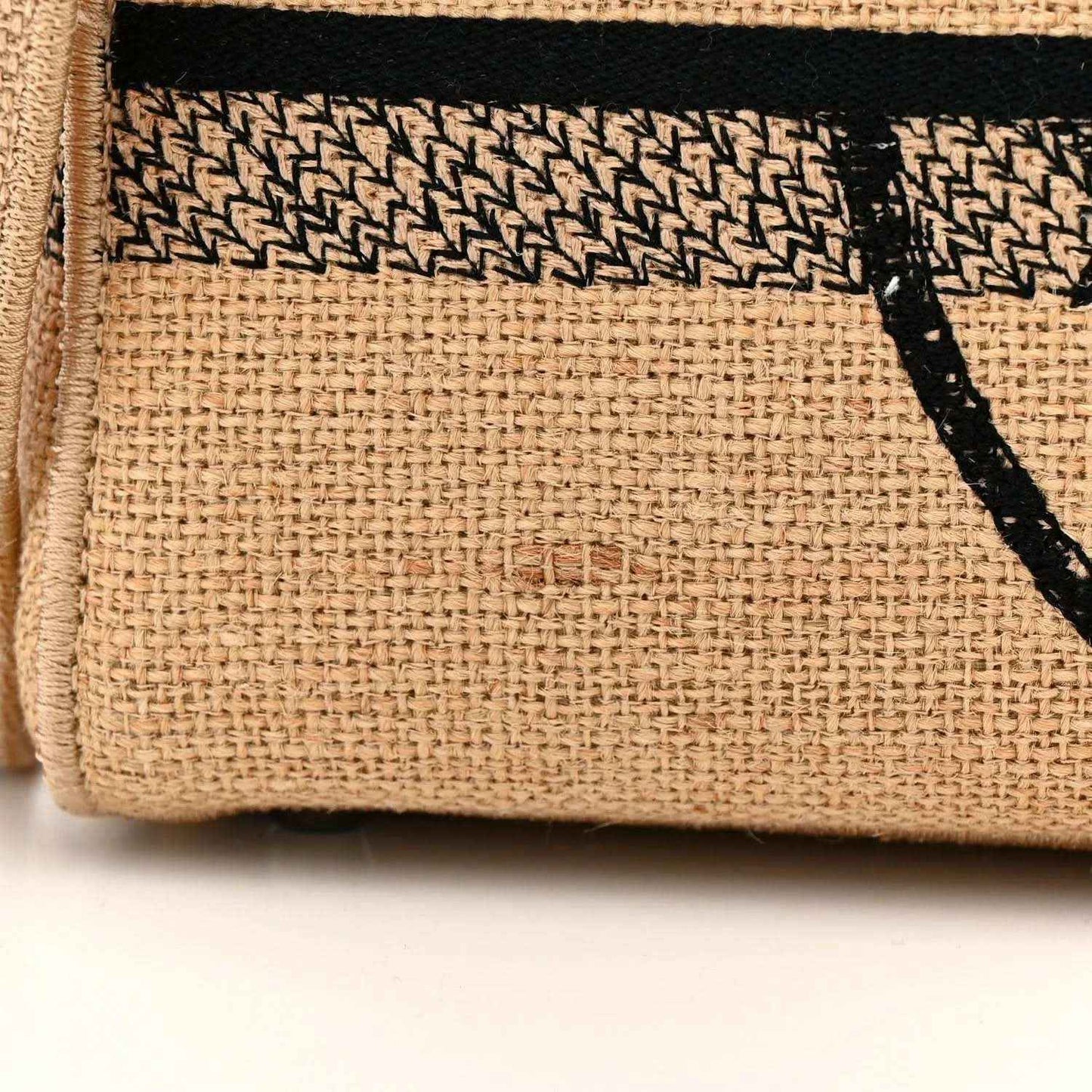 Beige jute tote bag fabric close-up with black logo stripe and woven texture