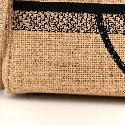 Beige jute tote bag fabric close-up with black logo stripe and woven texture