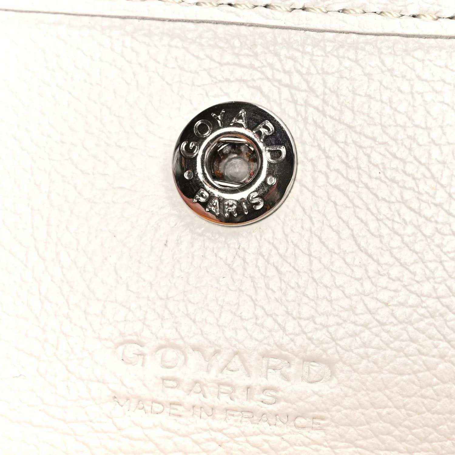 White pebbled leather strap end with round metal snap hardware labeled Goyard