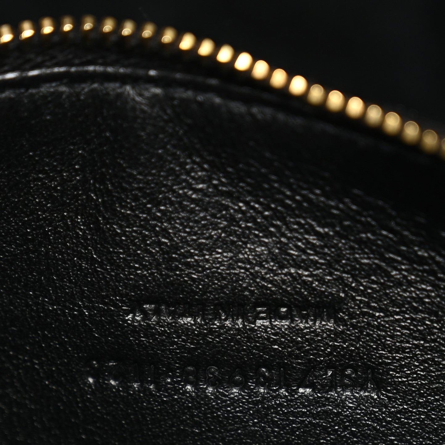 Close-up of black leather with subtle embossed text and gold zipper trim.