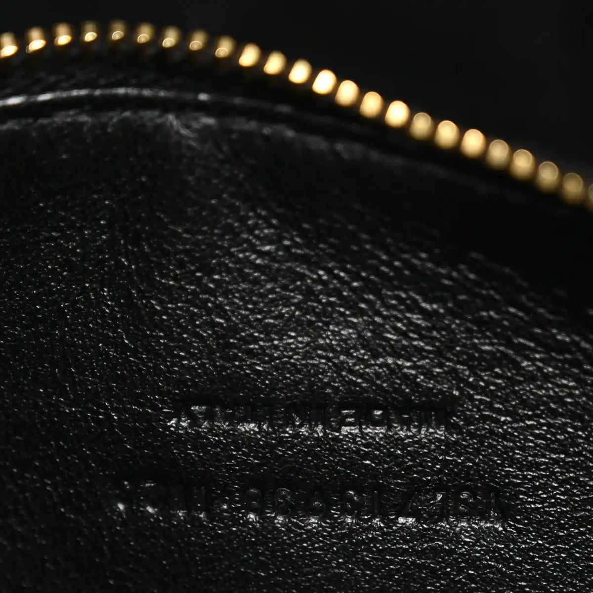 Close-up of black leather with subtle embossed text and gold zipper trim.