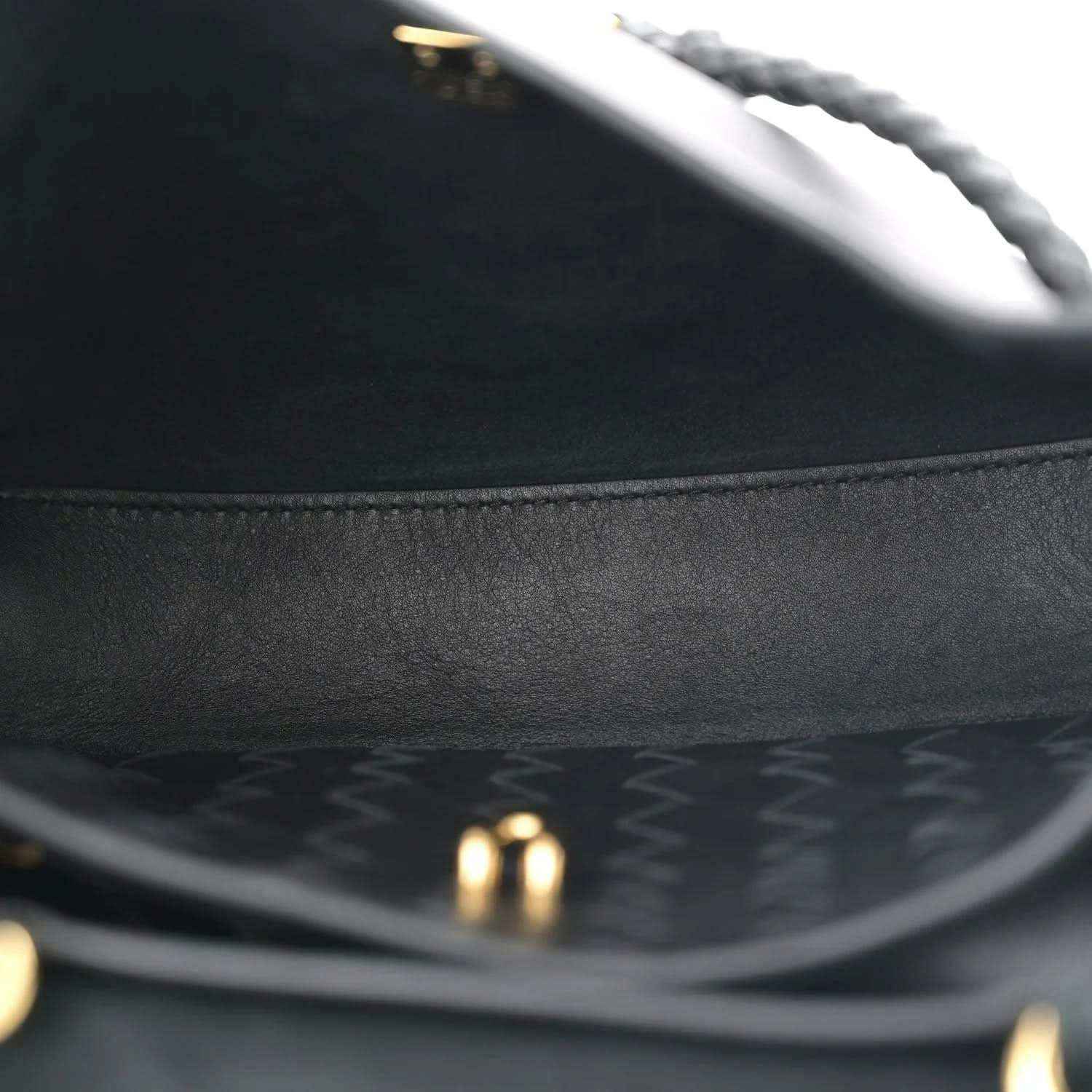 Black leather bag interior close-up with stitched edge and gold-tone hardware.