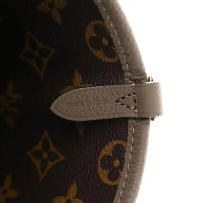 Monogram canvas bag strap end with gray leather tab and visible stitching detail