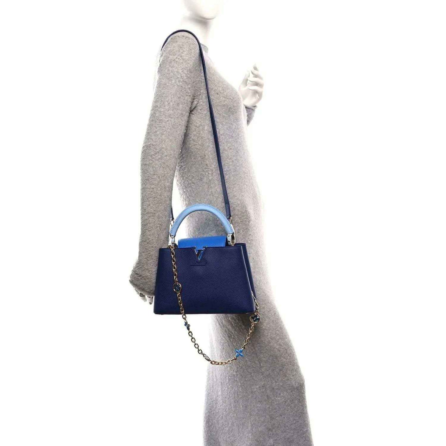 Blue handbag with top handle and small chain strap; shown from side on a model