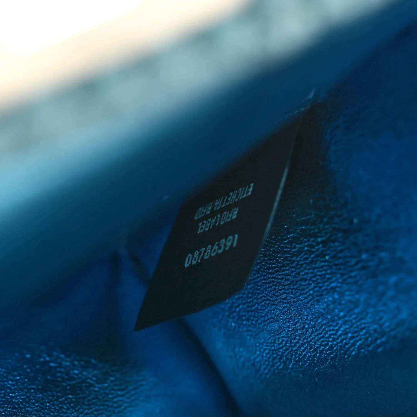 Blue leather satchel interior label patch with embossed text and serial number.
