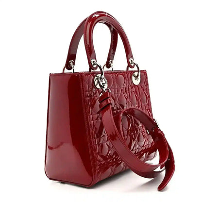Red patent leather handbag with top handles, bow strap detail, and silver hardware.