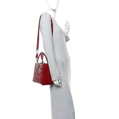 Red patent leather handbag with thin strap and silver hardware, side view.