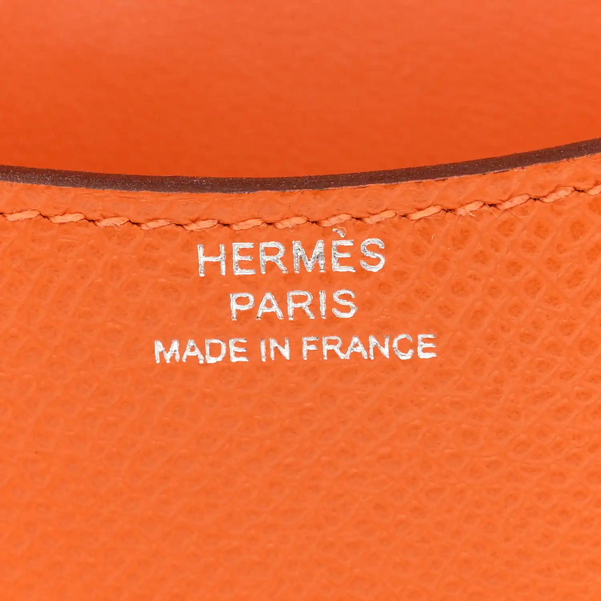 Hermes Paris Made in France stamp on orange leather slim wallet.