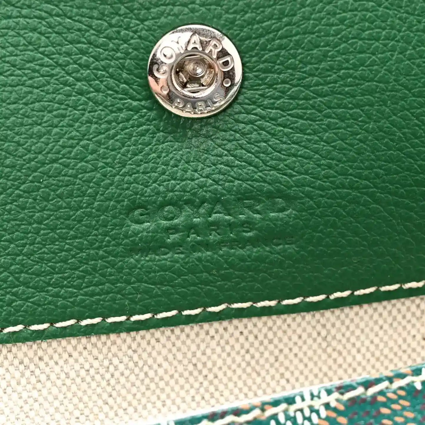 Green leather-like panel with circular metal snap and Goyard Paris logo