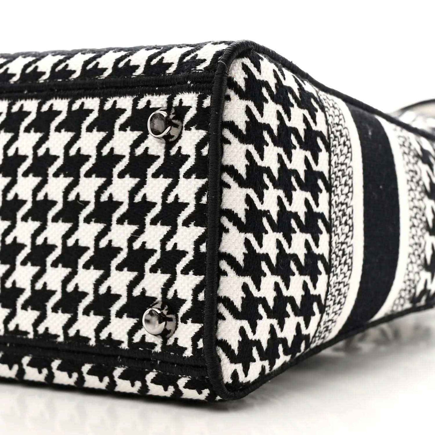 Black-and-white houndstooth canvas bag side with black trim, stud, and strap loop
