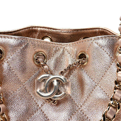 Close-up of copper quilted mini handbag front with CC-style logo and rings.
