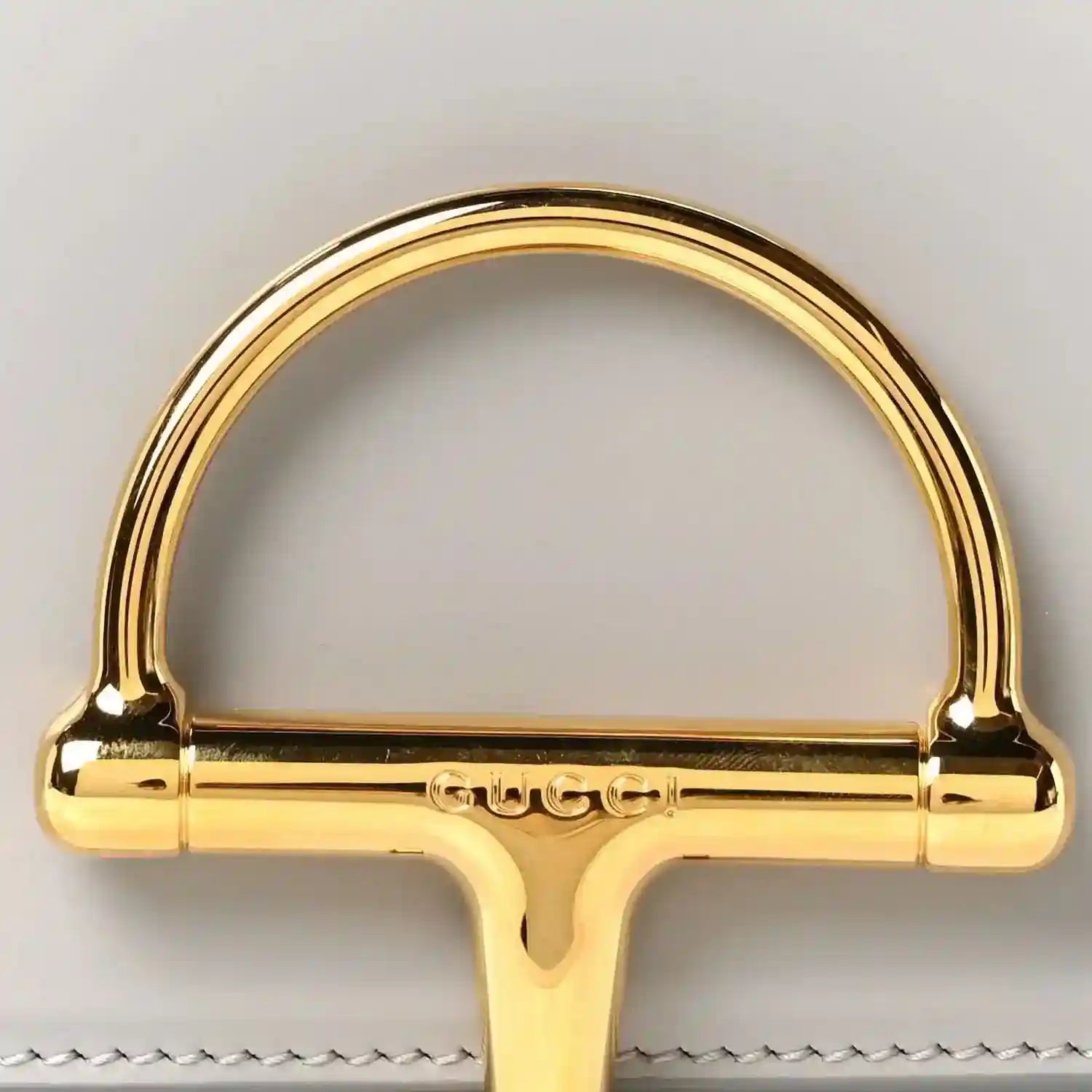 Gold-tone semicircle clasp hardware with Gucci engraving on light grey bag