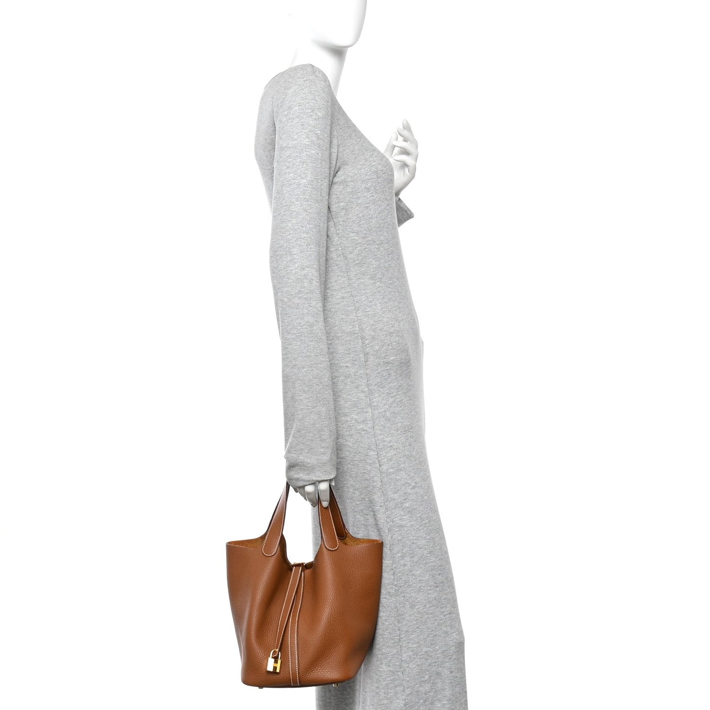 Tan leather bucket bag worn with a gray sleeve, cross-body hold