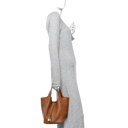 Tan leather bucket bag worn with a gray sleeve, cross-body hold