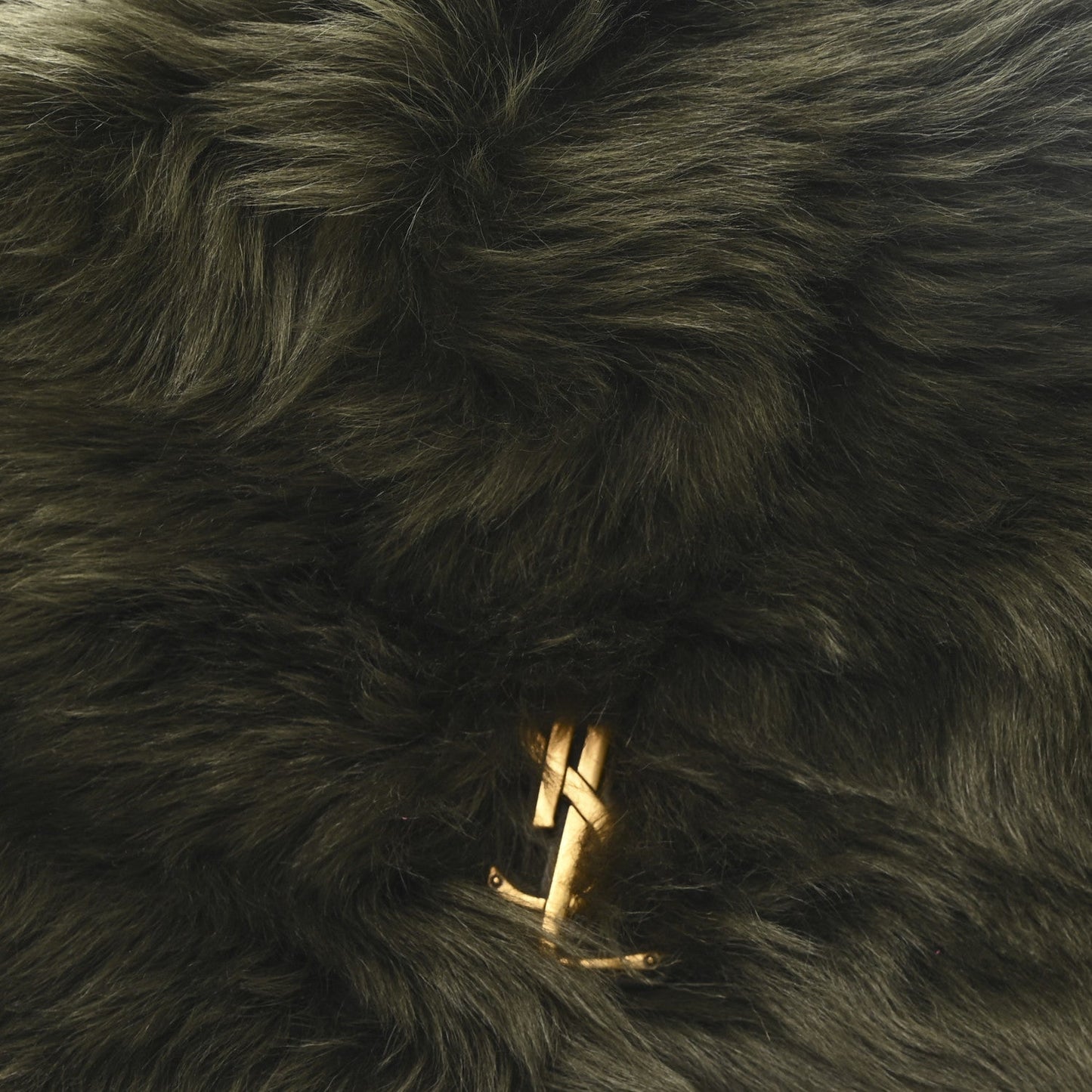 Dark olive shearling bag with gold YSL logo emblem on fur surface