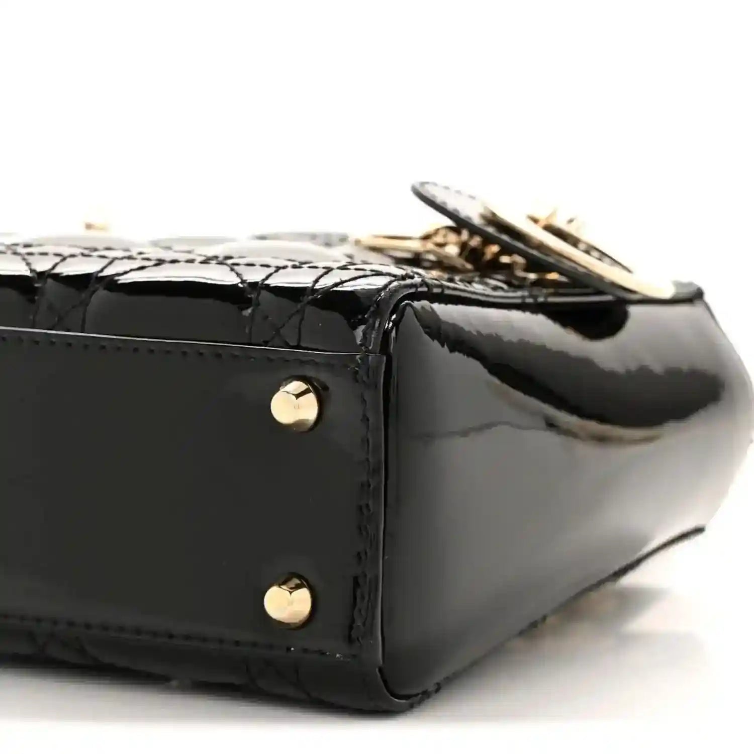 Black patent mini handbag close-up of side panel, gold rivets, and quilted trim