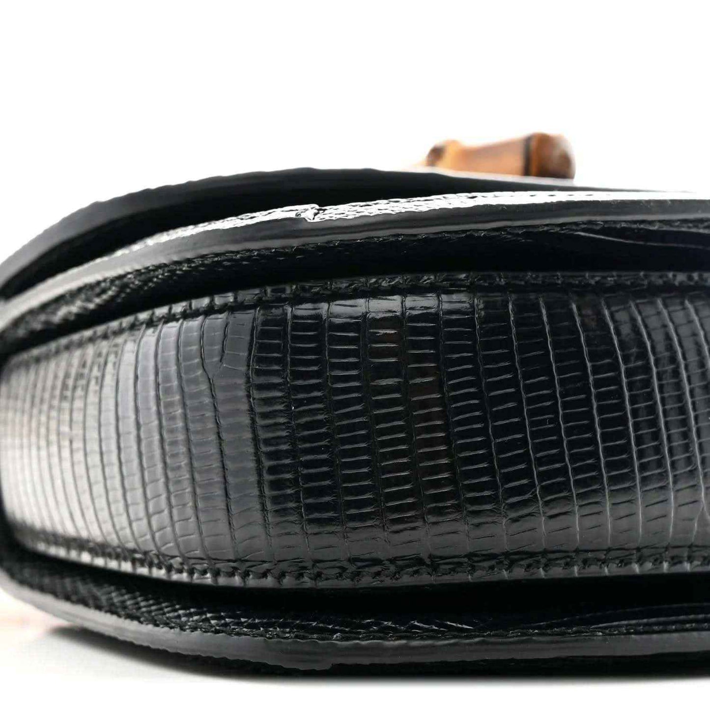 Close-up side of black mini bag with textured leather finish and curved edge