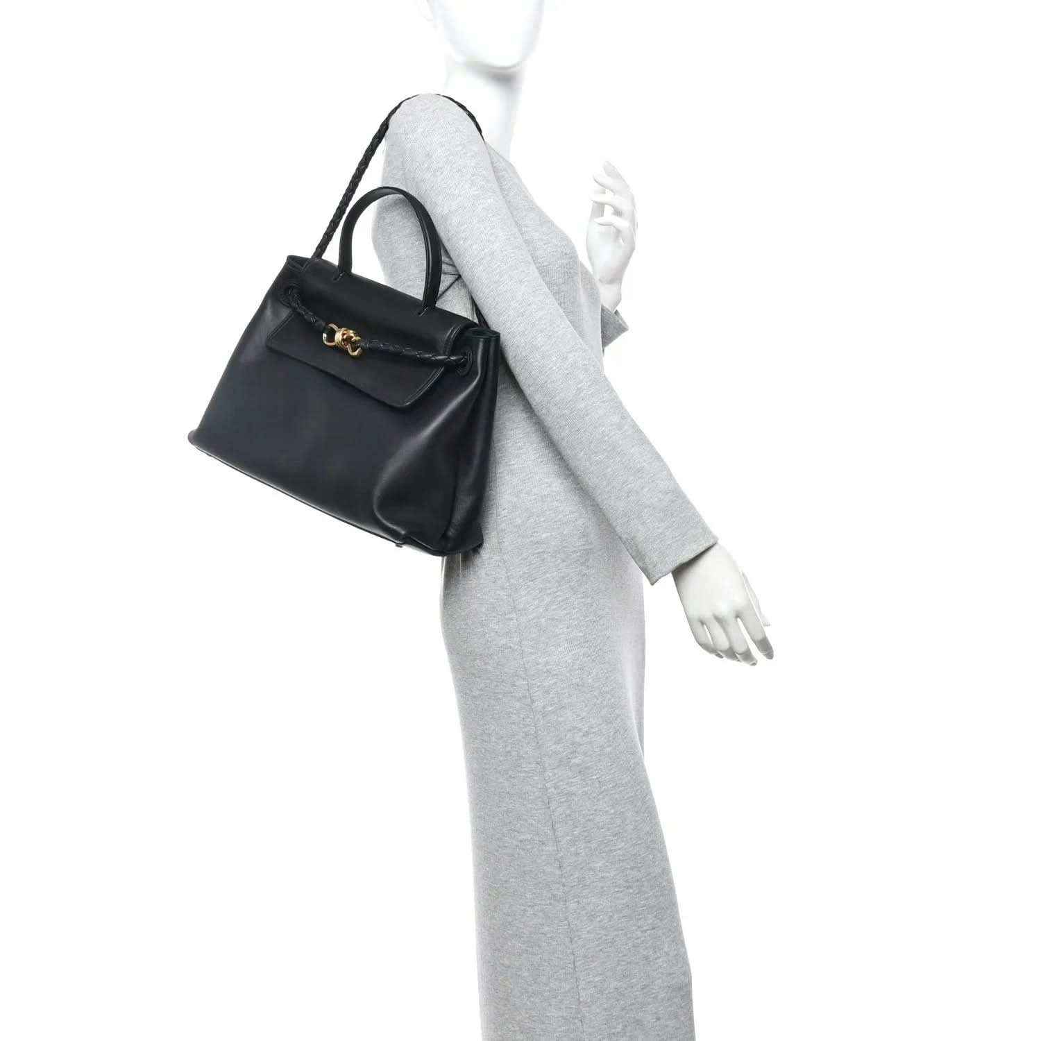 Black leather shoulder bag on model with front flap and braided shoulder strap.