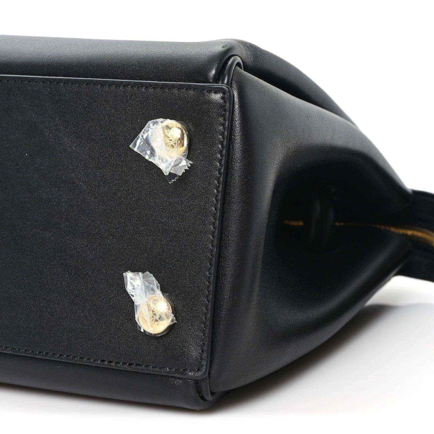 Black leather handbag corner with two gold-tone studs and stitched edge