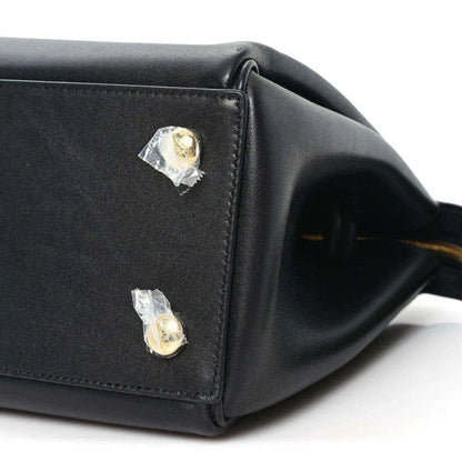 Black leather handbag corner with two gold-tone studs and stitched edge
