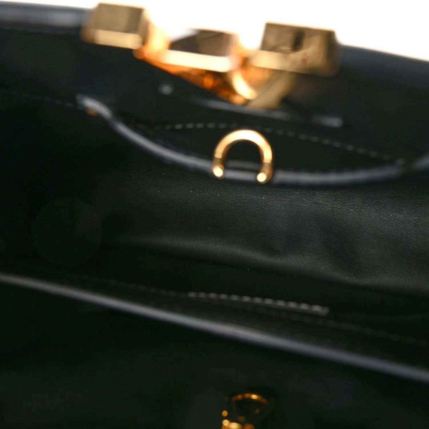 Close-up of black leather handbag strap with gold-tone ring hardware and stitching