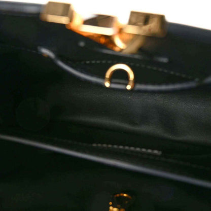 Close-up of black leather handbag strap with gold-tone ring hardware and stitching