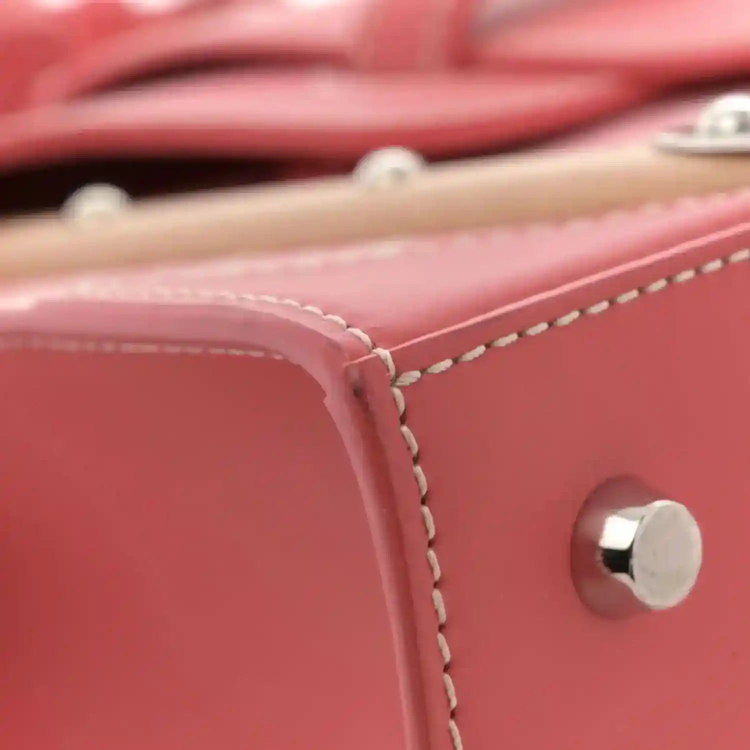 Pink leather bag edge with contrast stitching and round silver snap near strap.